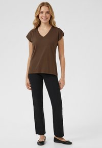 Brun, kortärmad V-ringad t-shirt kombinerad med svarta rakt skurna byxor och svarta ballerinaskor. Tröjan har en mjuk, len textur.