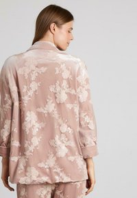 Top de pijama de terciopelo rosa con un diseño bordado floral, mangas largas y un corte holgado, con una tapeta de botones y cuello doblado.