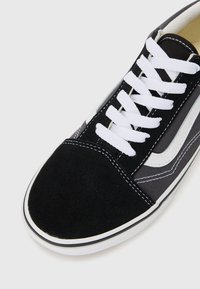 Schwarzer und grauer Sneaker aus Wildleder und Stoff, mit weißen Schnürsenkeln, einer abgerundeten Zehenpartie und weißen seitlichen Akzenten mit Nähdetails.