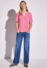 Rosa Kurzarmoberteil mit V-Ausschnitt, kombiniert mit weit geschnittenen blauen Denim-Jeans. Die Schuhe haben ein Leopardenmuster.