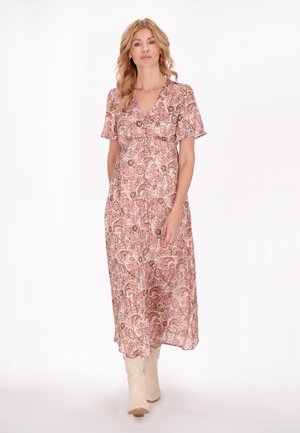 Maxi jurk in een roze paisley patroon, korte mouwen, V-hals, vloeiende stijl, lichtgewicht stof, gedragen met crème cowboylaarzen.