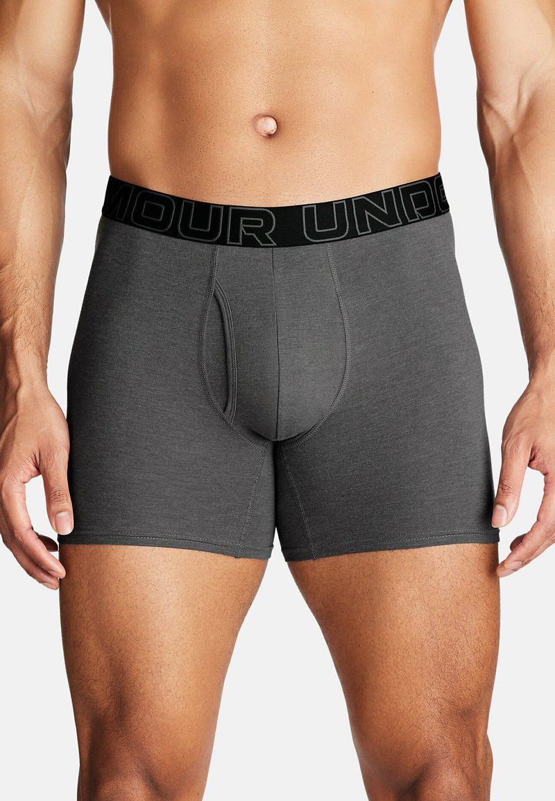 Šedé boxerky s černým pasem, na kterém je text "ARMOUR UNDER", elastický materiál a tvarovaný klín.