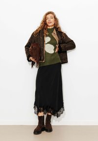 Veste en imprimé léopard marron, pull en tricot vert avec un motif blanc, jupe noire avec un ourlet en dentelle et bottines en suedine marron.