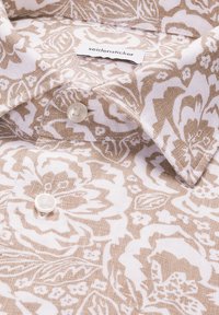 Col de chemise beige et blanche à motifs floraux boutonné avec étiquette de marque « seidensticker » visible sur tissu tissé.