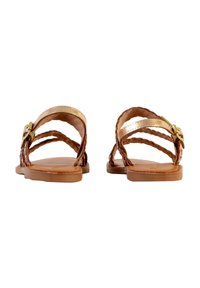 Sandalias de piel marrón con tiras trenzadas y un pequeño broche dorado. Suela plana con textura suave. La vista posterior muestra la disposición de las tiras.