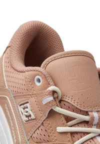Light pink athletic shoe with a textured leather and mesh upper, featuring white laces, perforated details, and a logo patch on the side.