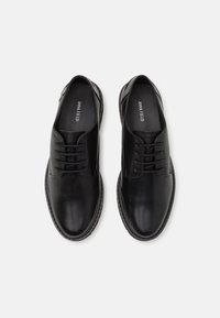 Chaussures à lacets en cuir noir avec une texture lisse, un bout arrondi et des coutures contrastées autour de la semelle. Design minimaliste.