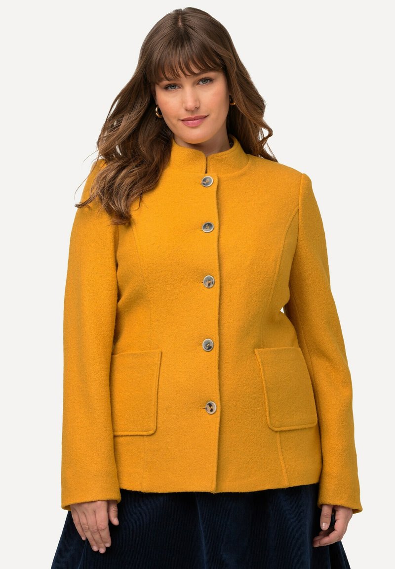 Giacca in fleece gialla con colletto rialzato, cinque bottoni, due tasche frontali e taglio dritto, caratterizzata da un tessuto morbido e testurizzato.