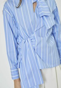 Hellbluse mit langen Ärmeln, gestreift, Wickeldesign, in der Taille gebunden und einem offenen Ausschnitt mit einer Schleifendetail. Glatte Stoff.