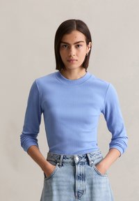Top de manga larga de color azul claro con ribetes y cuello redondo, combinado con pantalones cortos de mezclilla desgastados de tiro alto. Ambos artículos tienen bolsillos.