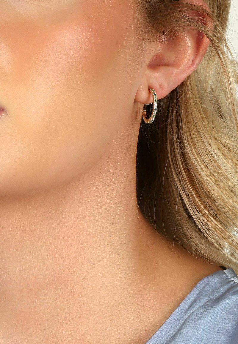 Guldtonade ringörhängen med klara rhinstenar längs kanten, små i storlek, med en polerad metallisk finish och cirkelformad design.