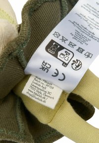 Stofmærke på en blød legetøj; har olivengrøn bomuld med lys beige og gule nuancer, vaskeanvisninger og brandoplysninger.