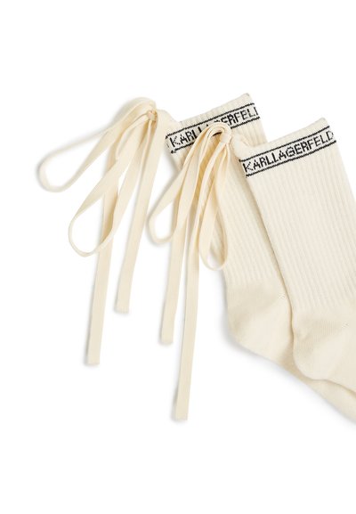 Chaussettes côtelées couleur crème avec texte noir « KARL LAGERFELD » au bord-côte et longs rubans en tissu noués à l’arrière.