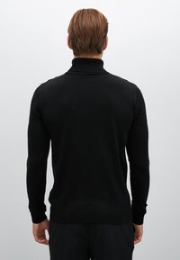 Zwarte gebreide trui met hoge kraag, met ribbeltextuur op de schouders en mouwen. Soepele stof met aansluitende boorden en zoom.