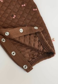 Brązowa, pikowana tkanina z wzorem wiśni. Wyposażona w srebrne zatrzaski i elastyczne mankiety zapewniające dopasowanie. Miękka w dotyku o gładkim wykończeniu.