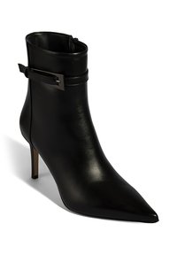 Bottine noire en cuir avec bout pointu, fermeture éclair latérale et fine sangle avec accent métallique à la cheville. Talon stiletto.
