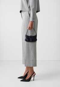 Svart läderhandväska med ett handtag upptill och en dekorativ spänne, i kombination med en grå och vit rutad kostym och svarta stiletto-klackar.