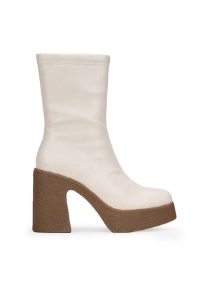 Bottes plateforme blanches en cuir, arrivant jusqu'au genou, avec un talon épais en brun texturé, présentant un dessus lisse et un design à bout rond.