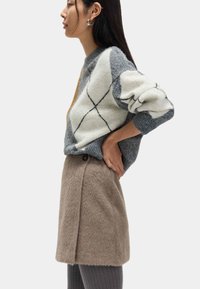 Grijs en crèmekleurig gebreide trui met een ontspannen pasvorm, gecombineerd met een beige textuurrijke minirok met een knoopdetail aan de zijkant.