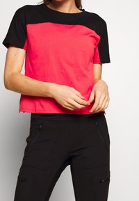 Koszulka z krótkim rękawem o jasnoróżowym korpusie i czarnych ramionach, wykonana z miękkiego materiału, o luźnym kroju. Zestawiona z czarnymi spodniami typu cargo.