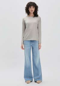 Hellgraues Langarm-Oberteil mit einem Boot-Ausschnitt, kombiniert mit lockeren, hellblauen Bootcut-Jeans. Sanfte Textur mit minimalen Designdetails.