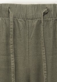 Μακριά παντελόνια από ελιά λινό με ελαστική μέση και κορδόνια από το ίδιο ύφασμα σε λευκό φόντο.