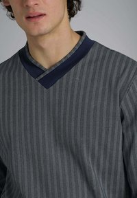 Maglietta a V con colletto blu navy, caratterizzata da un motivo a zigzag in tonalità scure e chiare. Tessuto morbido con una finitura testurizzata.