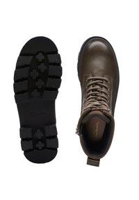 Botas de tobillo de cuero marrón con una superficie texturizada, ojales de metal y una suela de goma negra resistente con un patrón de tracción.