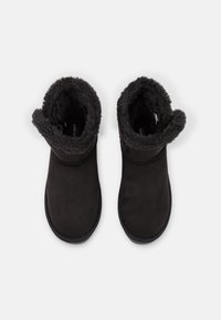 Un par de botas de invierno negras con forro suave y puntas redondeadas, mostradas desde arriba sobre un fondo blanco.