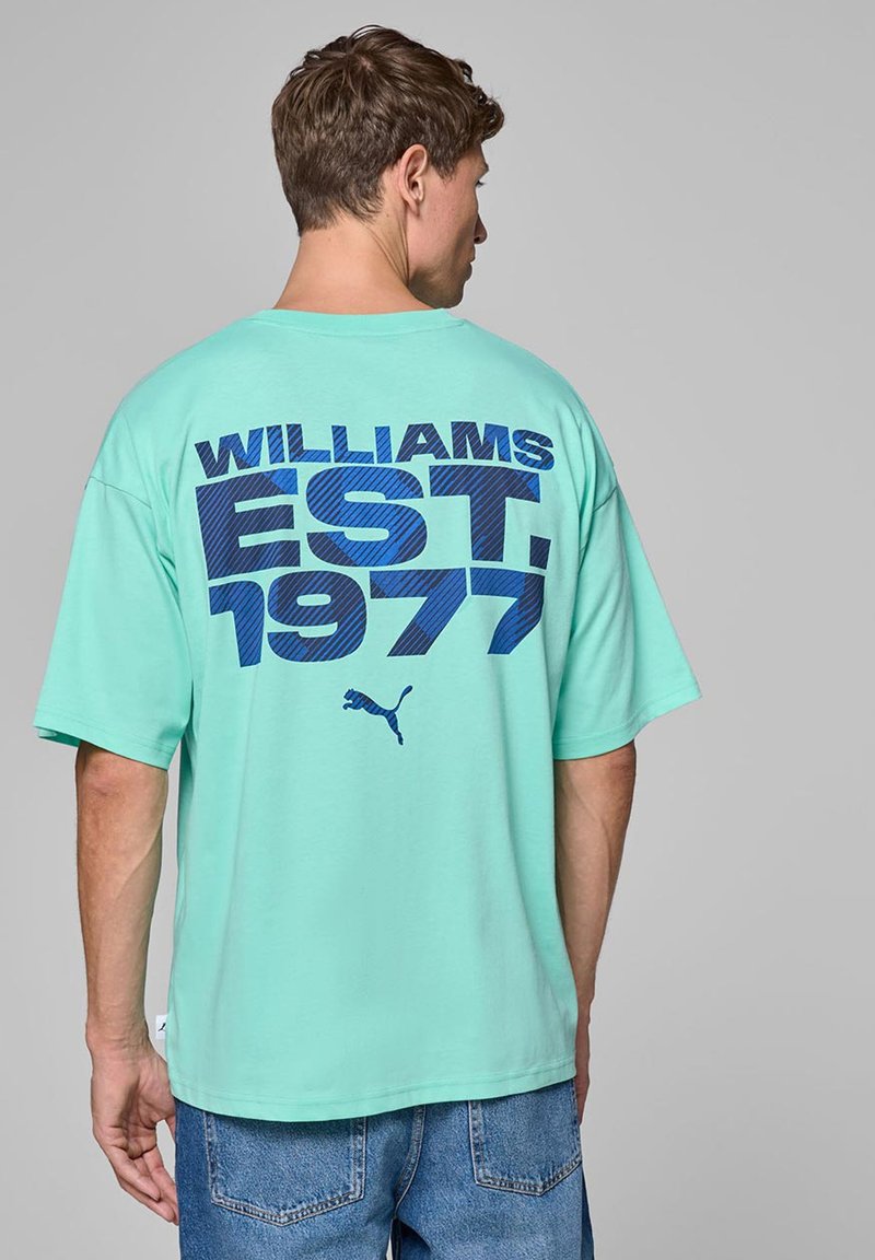 Turkusowa, oversize koszulka z krótkim rękawem, z odważnym niebieskim napisem „WILLIAMS EST. 1977” na plecach oraz małym logo Pumy, wykonana z bawełnianego materiału.
