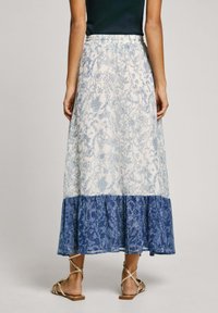 Vit kjol med blå blommönster, har en lagerdesign med en enfärgad blå nederkant. Elastisk midja. Bärs med beige sandaler med remmar.