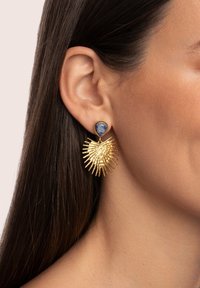 Pendientes en tono dorado con un diseño texturizado de rayos de sol, acentos en forma de pinchos y una piedra azul en forma de lágrima en la parte superior.