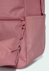 Mochila rosa hecha de un tejido texturizado con un lado suave y brillante. Cuenta con un bolsillo con cremallera y herrajes para correas ajustables.