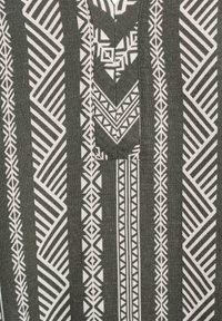 Tessuto decorato con un design geometrico bianco su uno sfondo verde scuro, con varie forme e linee che creano una texture visiva distintiva.