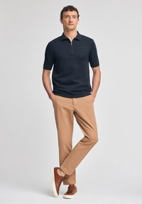 Mörkblå pikétröja med korta ärmar och dragkedjekrage, kombinerad med tanfärgade byxor och bruna sneakers. Slät textur och skräddarsydd passform.