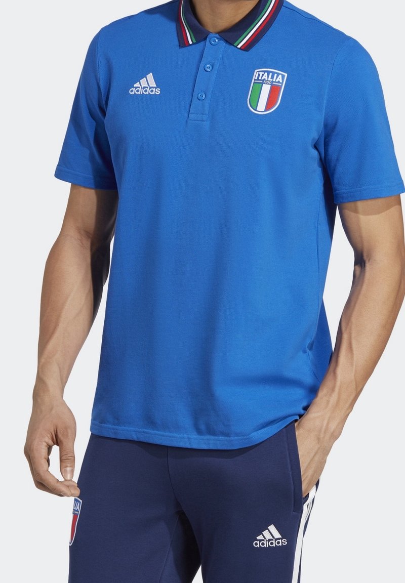 Homme portant un polo Adidas bleu avec le logo de l'équipe nationale de football d'Italie et un pantalon Adidas bleu assorti avec des bandes blanches et des logos.