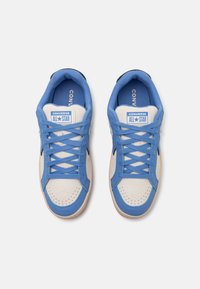 Adidași Blue Converse All Star cu vârful din suede crem, talpă din cauciuc și șireturi texturate. Prezintă eticheta brandului pe limbă.