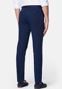 Granatowe bawełniane spodnie o dopasowanym kroju, charakteryzujące się gładką fakturą, szlufkami na pasek oraz tylnymi kieszeniami z detalami w postaci guzików.
