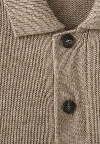 Beige gebreid vest met een geribde kraag, twee zwarte knopen en een gestructureerde stof met een zichtbaar steekpatroon.