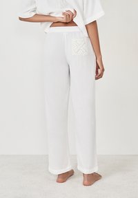 Witte, loszittende broek gemaakt van lichtgewicht stof, met een textuur gehaakte zak op de achterkant. De zoom is iets omgeslagen. Models in blote voeten.