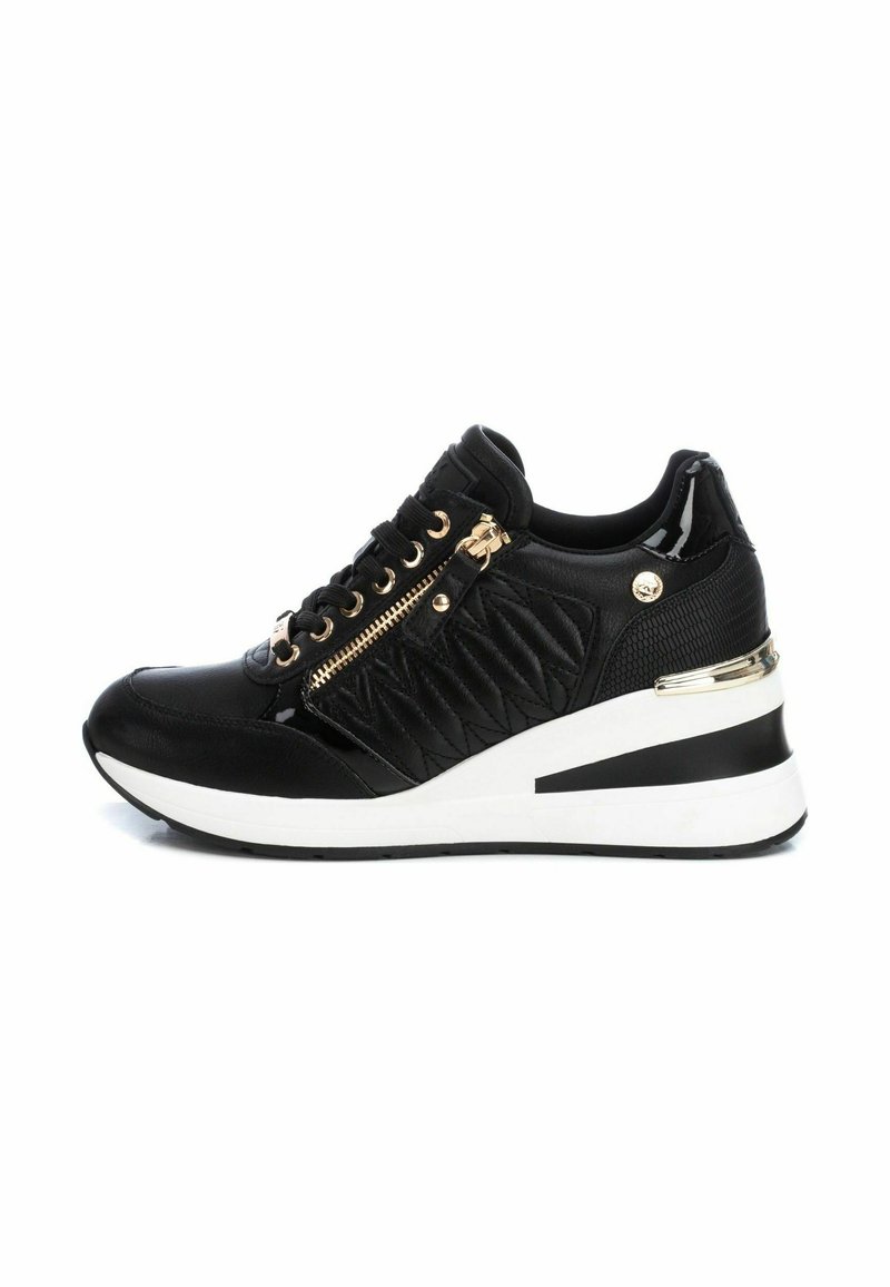 Las zapatillas negras presentan un diseño acolchado, acentos metálicos, cremallera lateral y una suela de cuña blanca gruesa con una franja negra.
