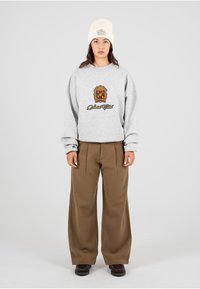 Grijze sweatshirt met logo, oversized pasvorm en geribde manchetten. Bruine wijde broek met een gladde textuur. Crème gebreide beanie met een patch.
