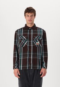 Long-sleeve plaid shirt in brown, teal, and white. Features two chest pockets and a branded label. Made of a soft, textured fabric.