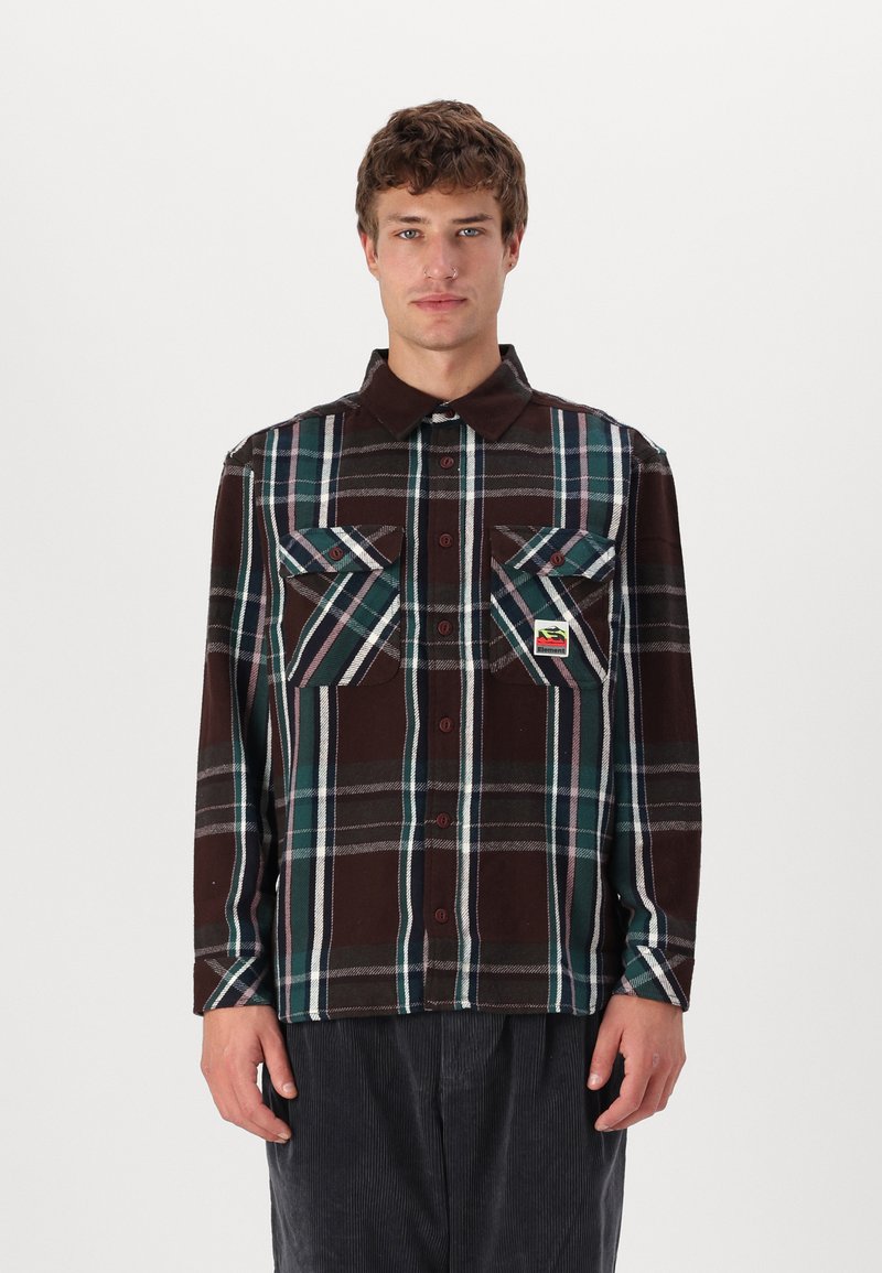 Long-sleeve plaid shirt in brown, teal, and white. Features two chest pockets and a branded label. Made of a soft, textured fabric.