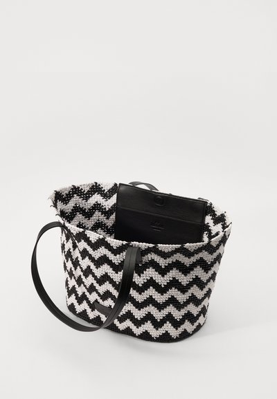 Στρογγυλή πλεκτή τσάντα με μαύρο και άσπρο διαγώνιο σχέδιο, μαύρες δερμάτινες λαβές και μια μικρή μαύρη θήκη μέσα. Υφασμάτινο, ανθεκτικό υλικό.