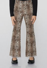 Beige flared kalhoty s leopardím potiskem a černými akcenty, s pěti kapsami a roztrhanými lemy, doplněné černými baletními plošinami.