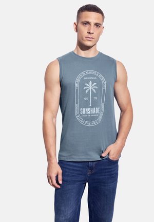 Mouwloze blauw-groene katoenen t-shirt met witte grafische tekst en een palmbomenontwerp op de voorkant. Casual pasvorm, gecombineerd met blauwe denim jeans.