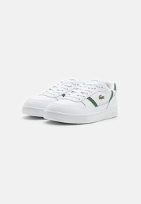 White sneakers with green accents, made from smooth synthetic material. Features include a perforated design, round toe, and textured sole.