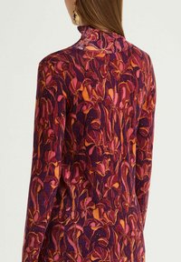 Pullover a maniche lunghe con collo alto, realizzato in tessuto strutturato con sfondo viola e motivo floreale arancione.