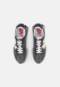 Grå och marinblå träningsskor med ett nätövre, platta snörningar, en texturerad sula och en röd logotyp på en ljusblå innersula.